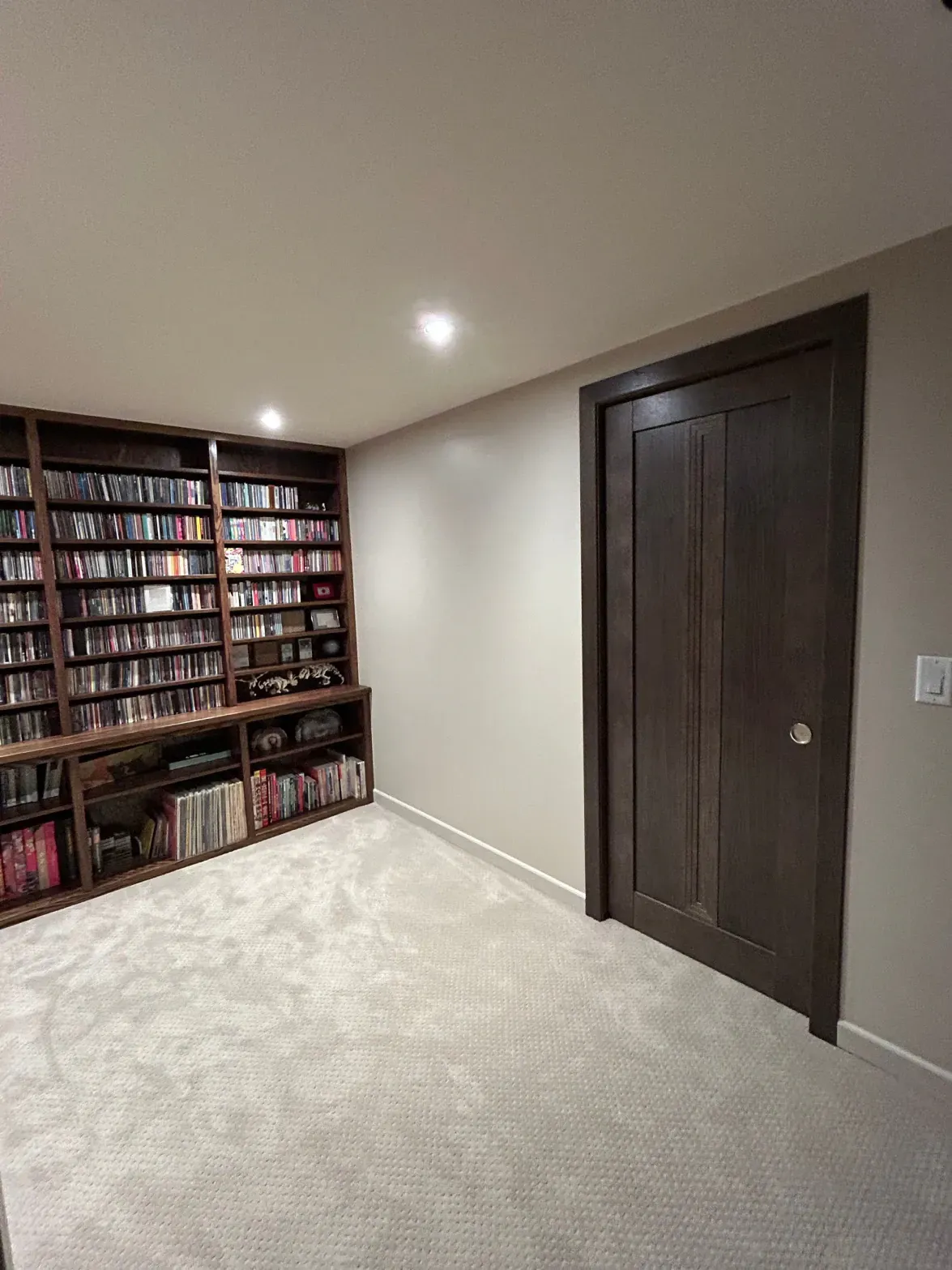 Carpeted room with built-in bookshelf and dark wood closet doors under recessed ceiling lights