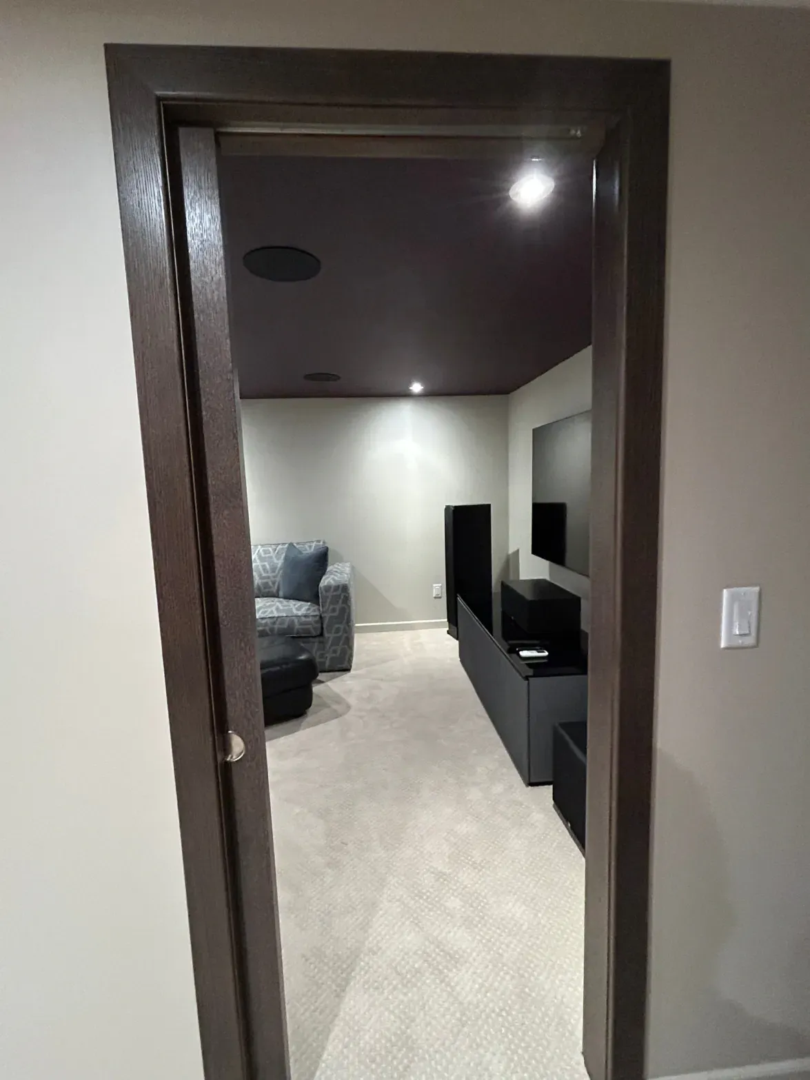 Doorway to a modern living room with gray sofa, TV console, and recessed lighting