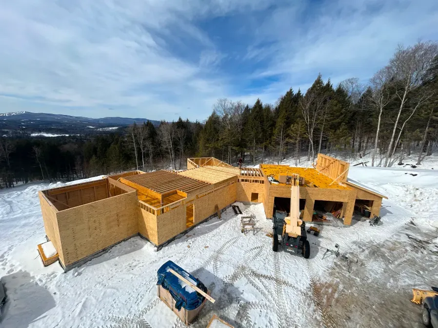 Snowy construction site with wooden house framing and a blue machine under a bright sky