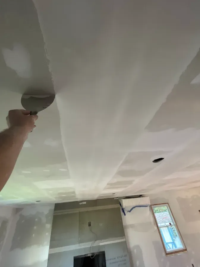 Hand smoothing drywall compound on a ceiling in a room under renovation