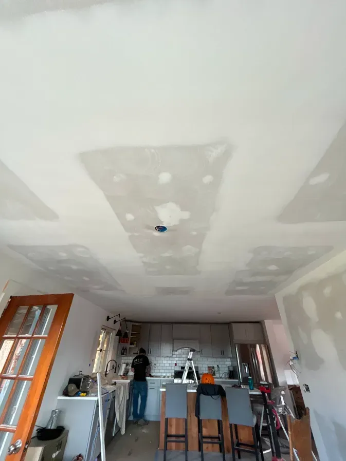 Renovation scene in a room with patched drywall ceiling, ladder, and tools near a kitchen island