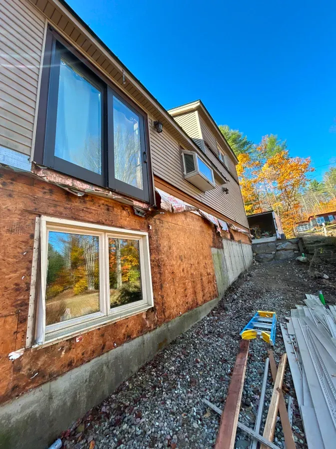 House exterior with new siding and windows, gravel yard, and stacked materials along the foundation