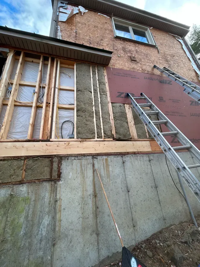 Partially renovated brick house with exposed framing, insulation, and a ladder leaning against the wall