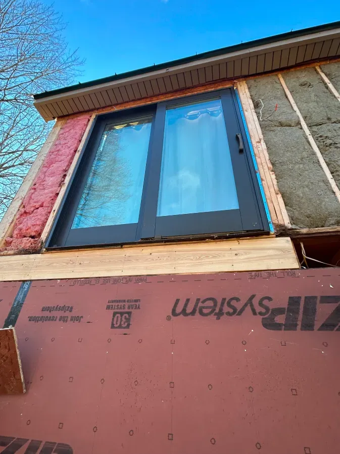 Window installed above exposed house siding with pink insulation board under a blue sky