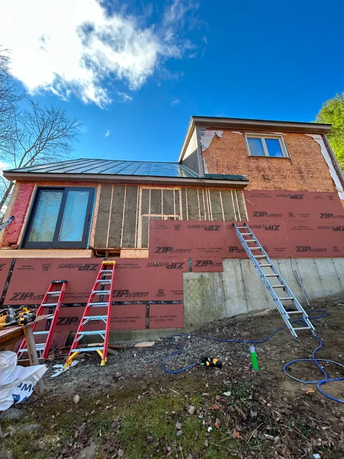 House under renovation with ladders against red exterior walls and solar panels on the roof