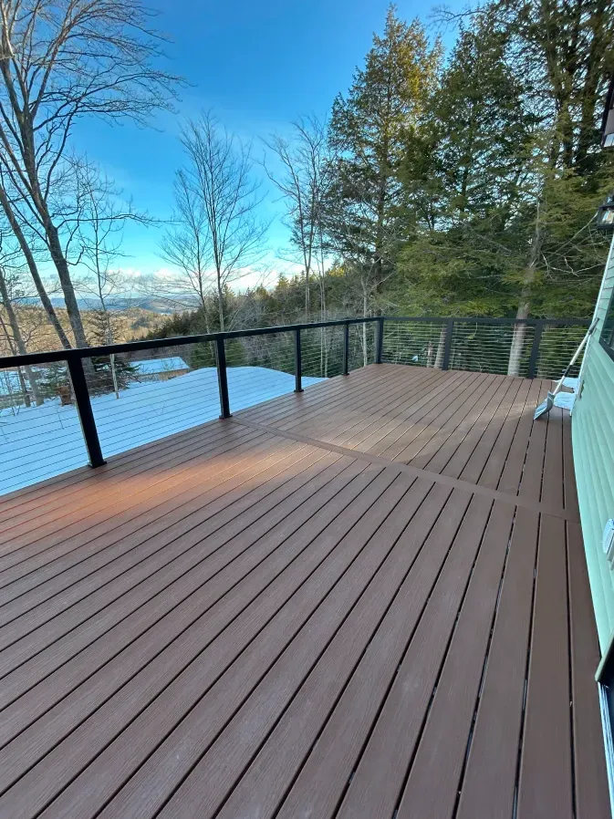 Wooden deck overlooking a calm lake and trees under a clear blue sky