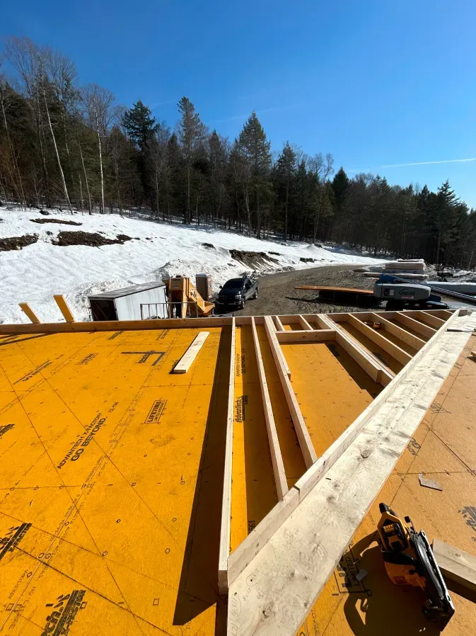 Construction site with yellow plywood framing on a snowy hillside under a blue sky