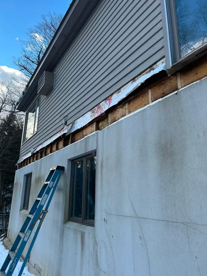 House exterior with a ladder leaning against unfinished siding above a concrete foundation