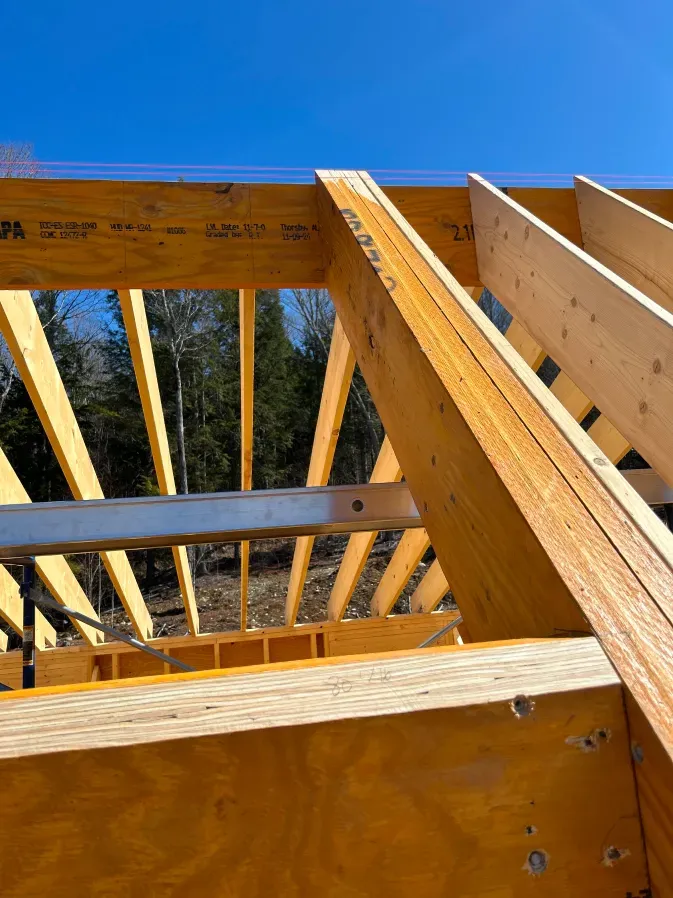 Wooden roof framing under construction against a clear blue sky.