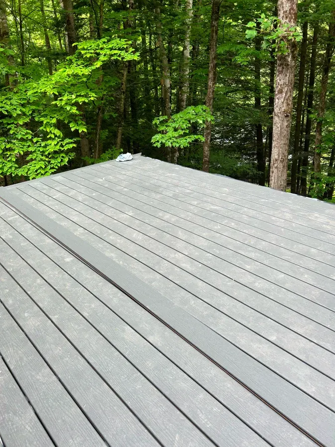 Gray wooden deck overlooking a green forest with tall trees and lush foliage