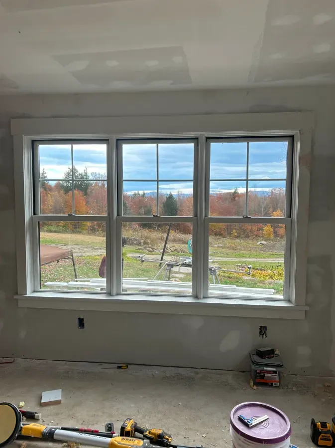 Partially renovated room with a large white window overlooking a grassy yard and autumn trees