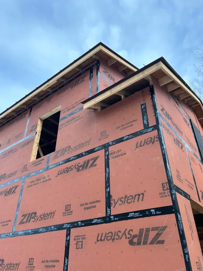 Partially wrapped pink house under construction against a blue sky