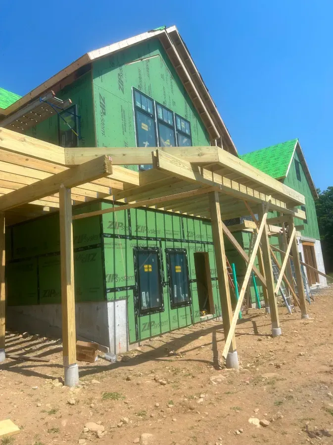 Green house under construction with wooden porch framing and a blue sky background