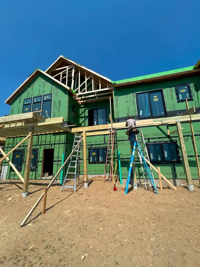 Two-story green house under construction with scaffolding against a blue sky