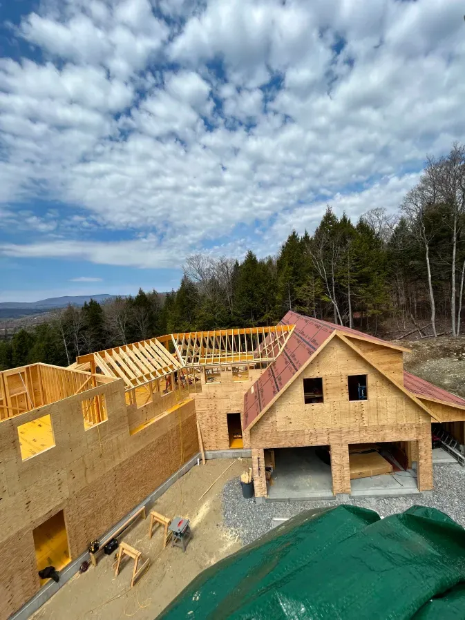 Partially framed house under construction with plywood walls, roof trusses, and a cloudy sky above