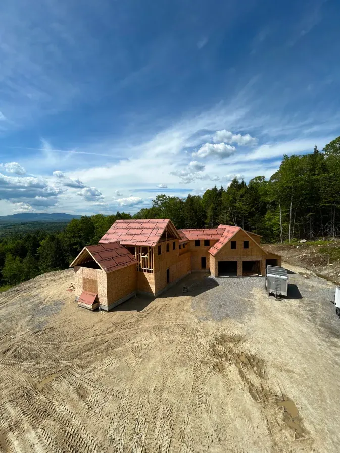 Partially built house with red roofs on a cleared hillside under a blue sky