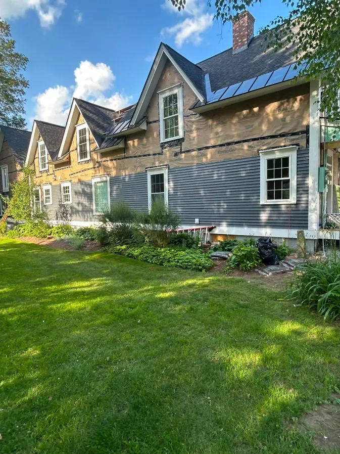Stone house with gabled dormers, gray siding, and a green lawn under a bright blue sky