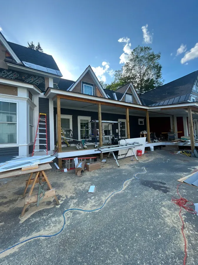 Partially built house exterior with scaffolding, ladders, and construction materials in the driveway