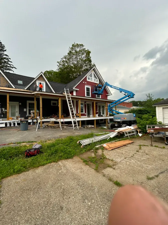 House under renovation with scaffolding, ladders, and a blue lift truck in the yard