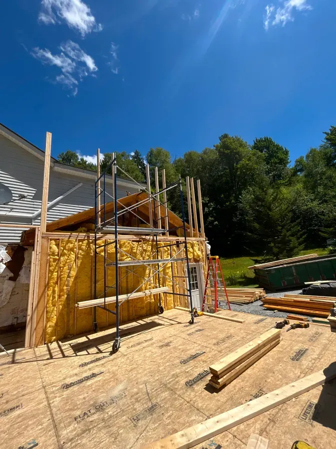 Scaffolding around a yellow house under construction, with lumber and tools on a sunny day.