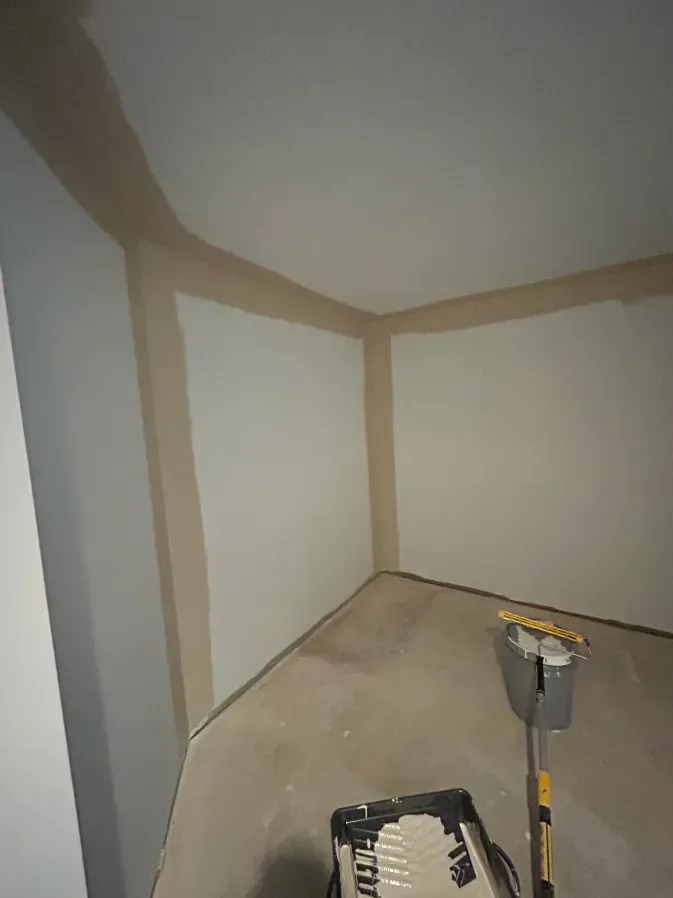 Empty corner of a room with unfinished drywall, a floor tool, and a small container on the floor.