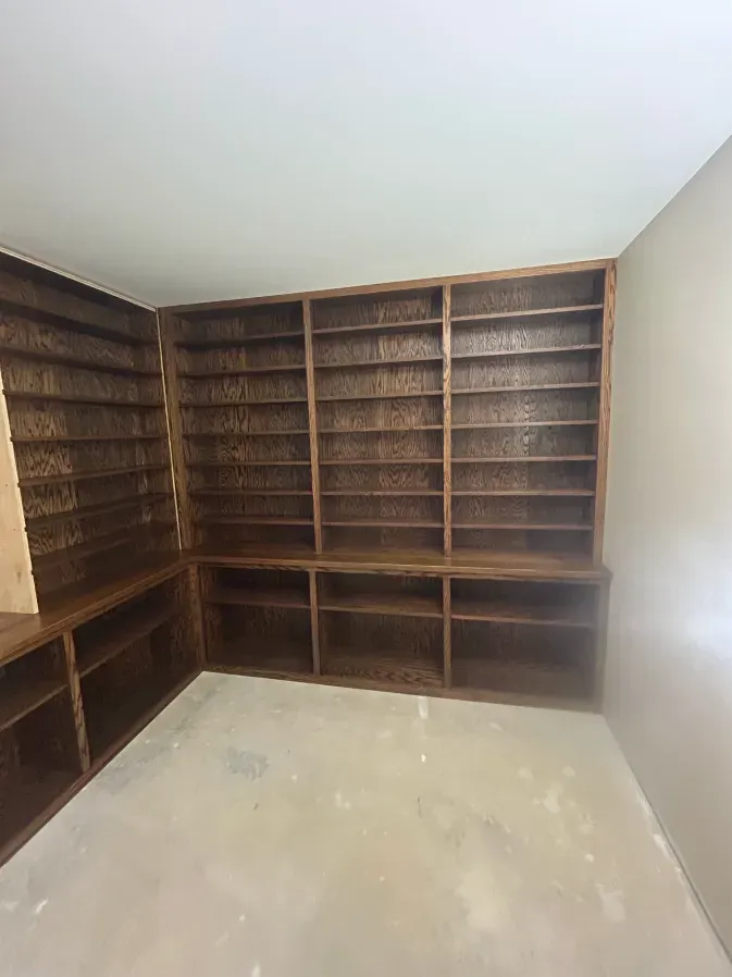 Empty room with built-in dark wood bookshelves on two walls and a bare floor.
