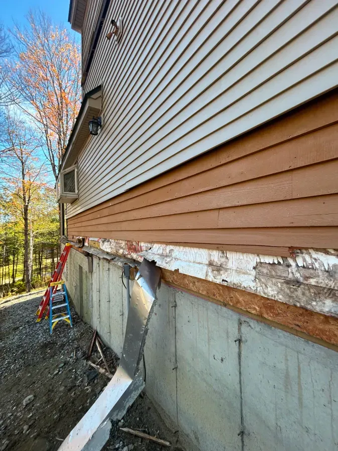 House exterior with damaged siding and exposed foundation, showing ongoing repair work.