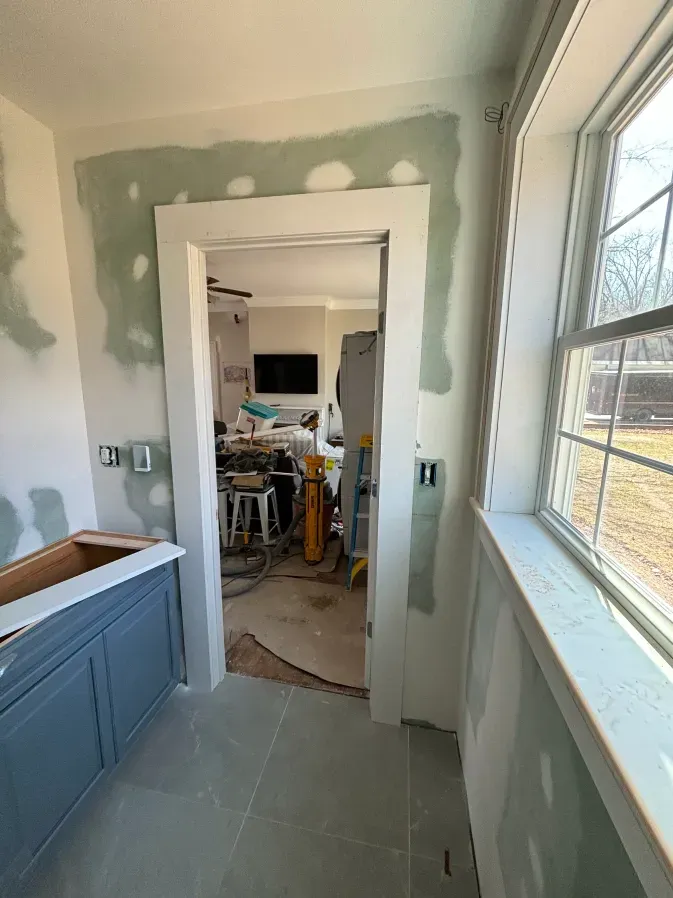 Partially renovated room with green drywall patches, blue cabinet, and doorway to a cluttered adjoining room