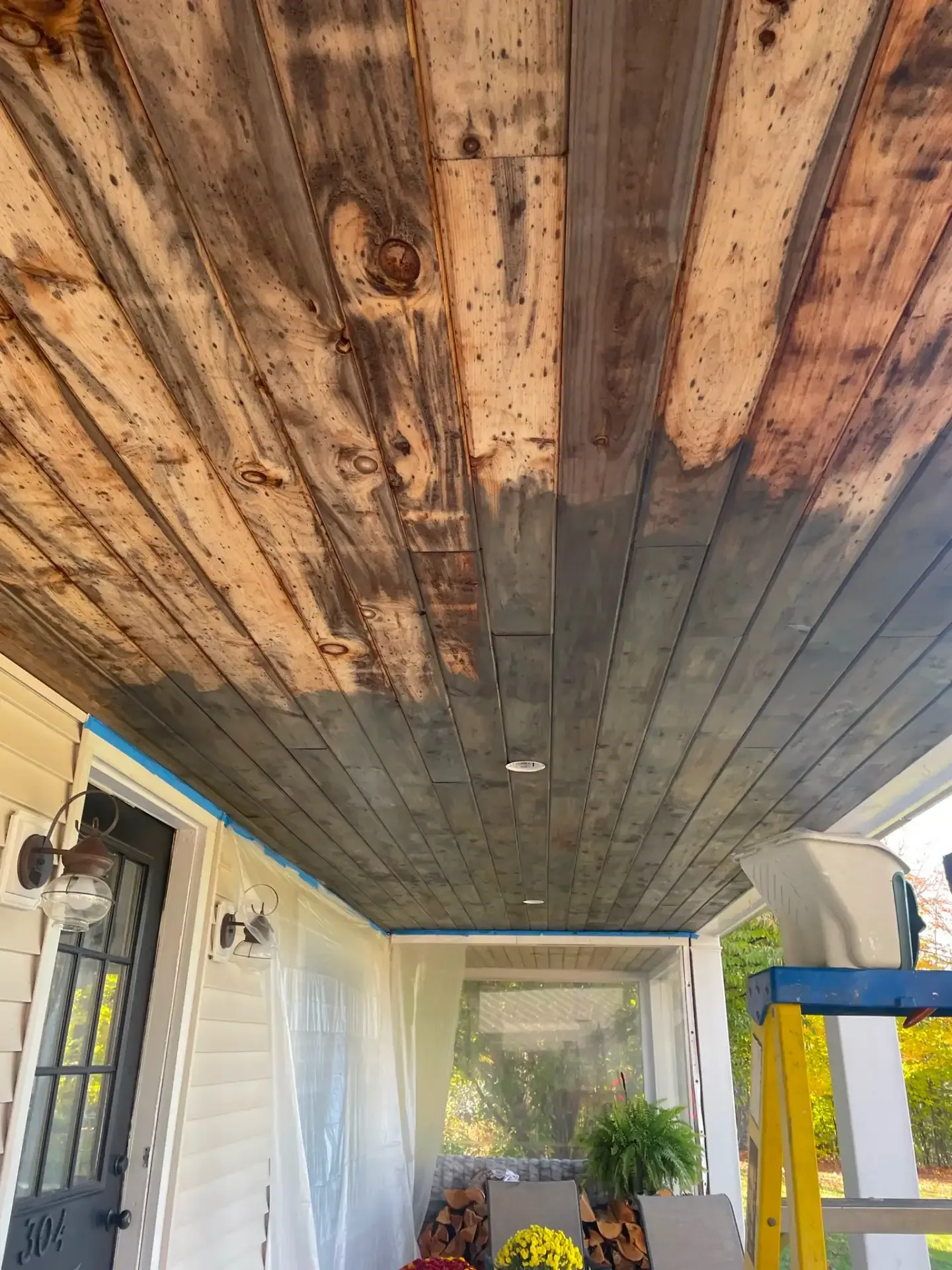 Wooden porch ceiling with dark water stains, overlooking a covered patio and exterior doorway