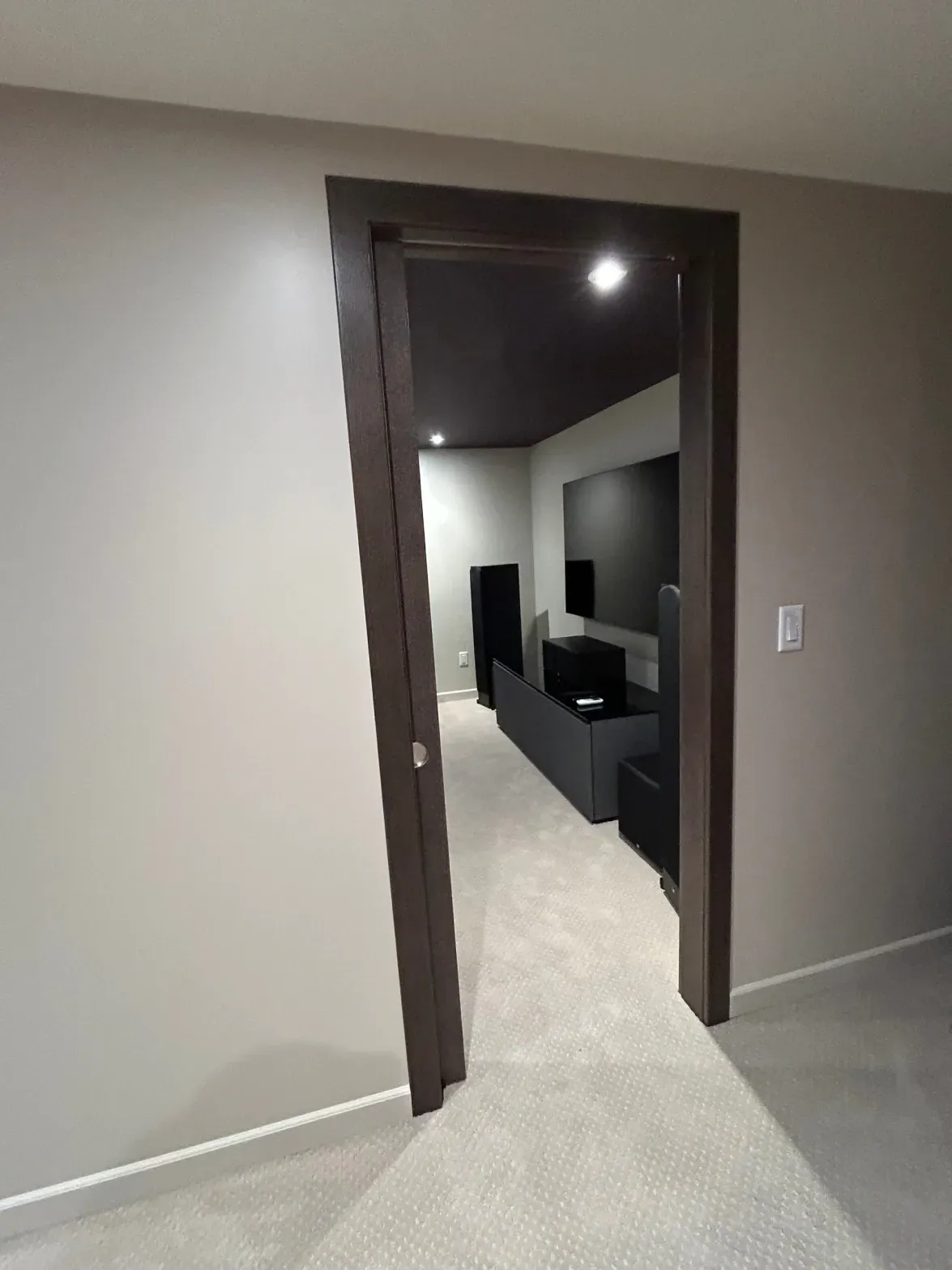 Hallway entrance to a dark modern media room with black furniture and a wall-mounted TV
