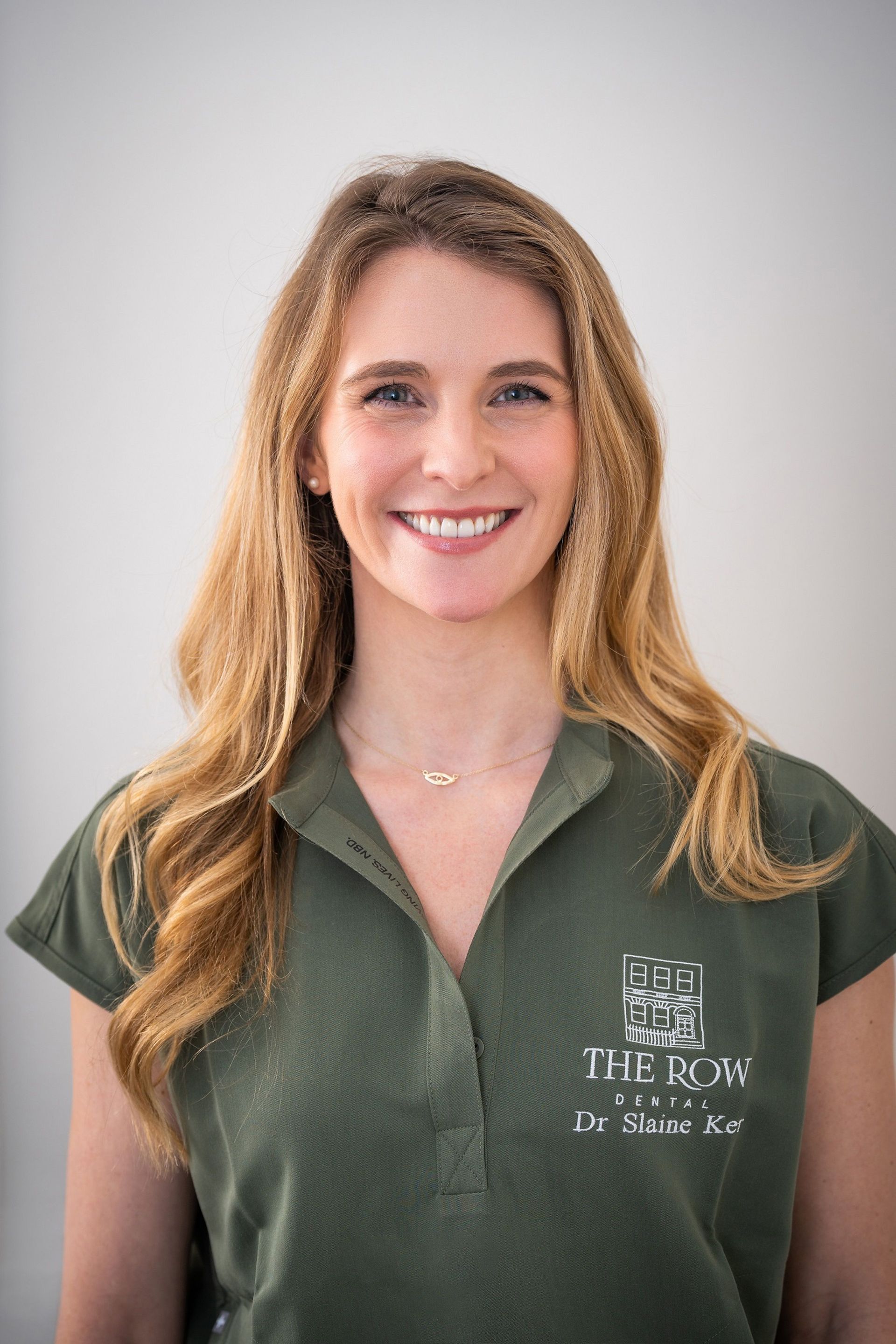 Smiling person in a green polo shirt standing against a light gray background