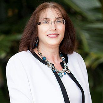Wanda Davis Portrait of a smiling woman in a white blazer and black top, wearing glasses and a blue beaded necklace.