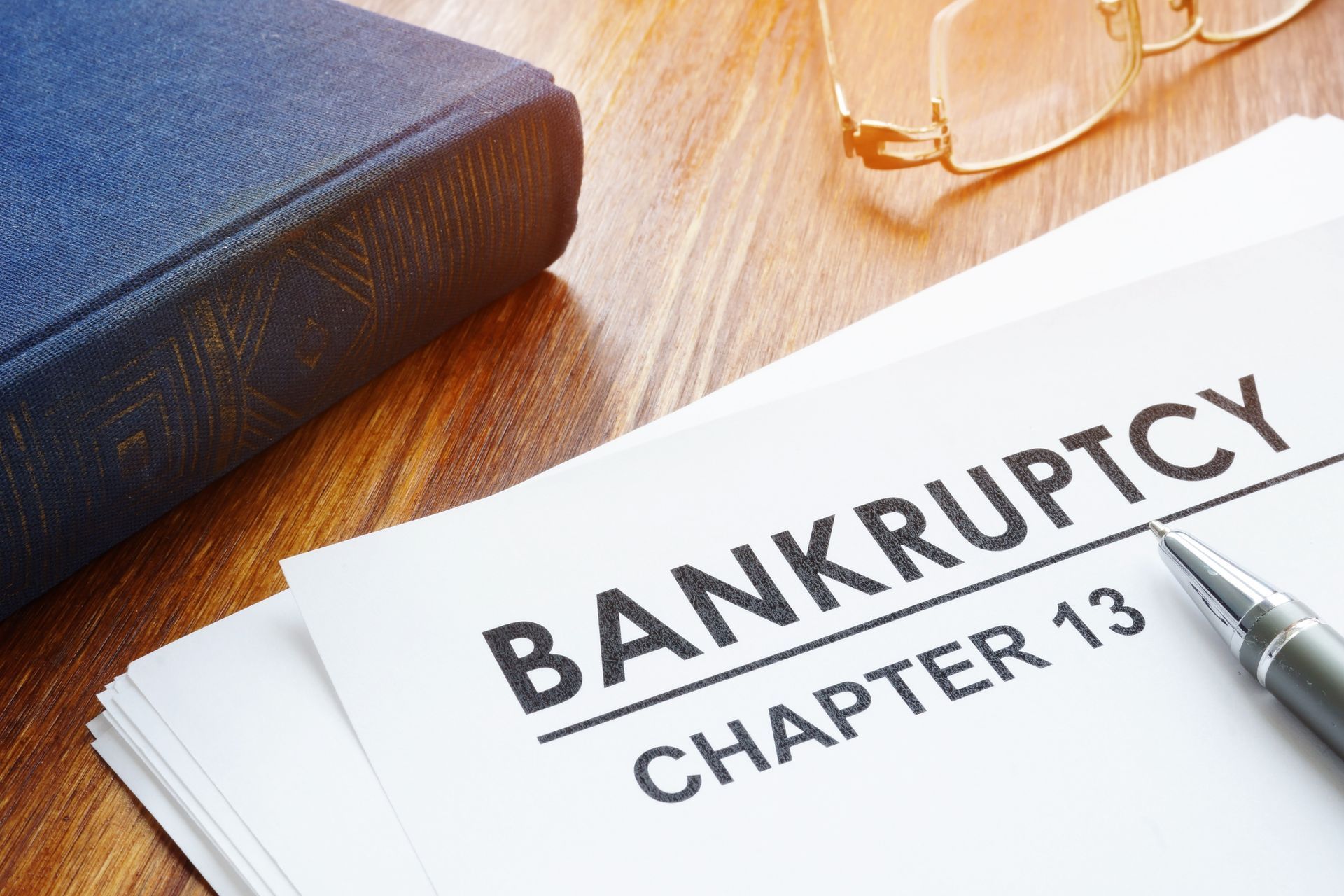 Bankruptcy Chapter 13 documents with pen, law book, and eyeglasses on desk.