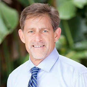 Drake Ozment Portrait of a man in a light blue shirt and striped tie smiling outdoors with blurred greenery