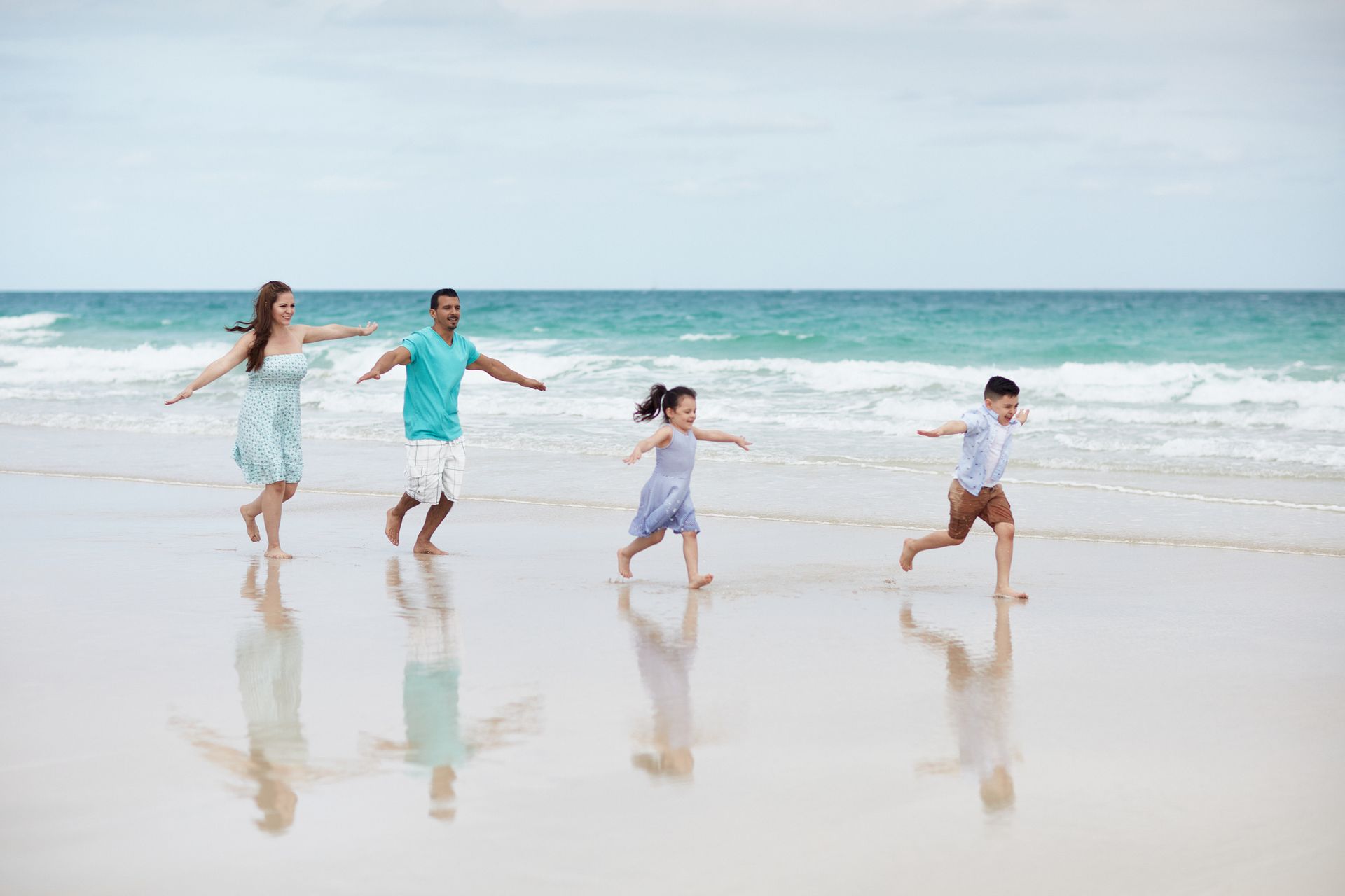 Four people running barefoot along a sunny beach with waves in the background