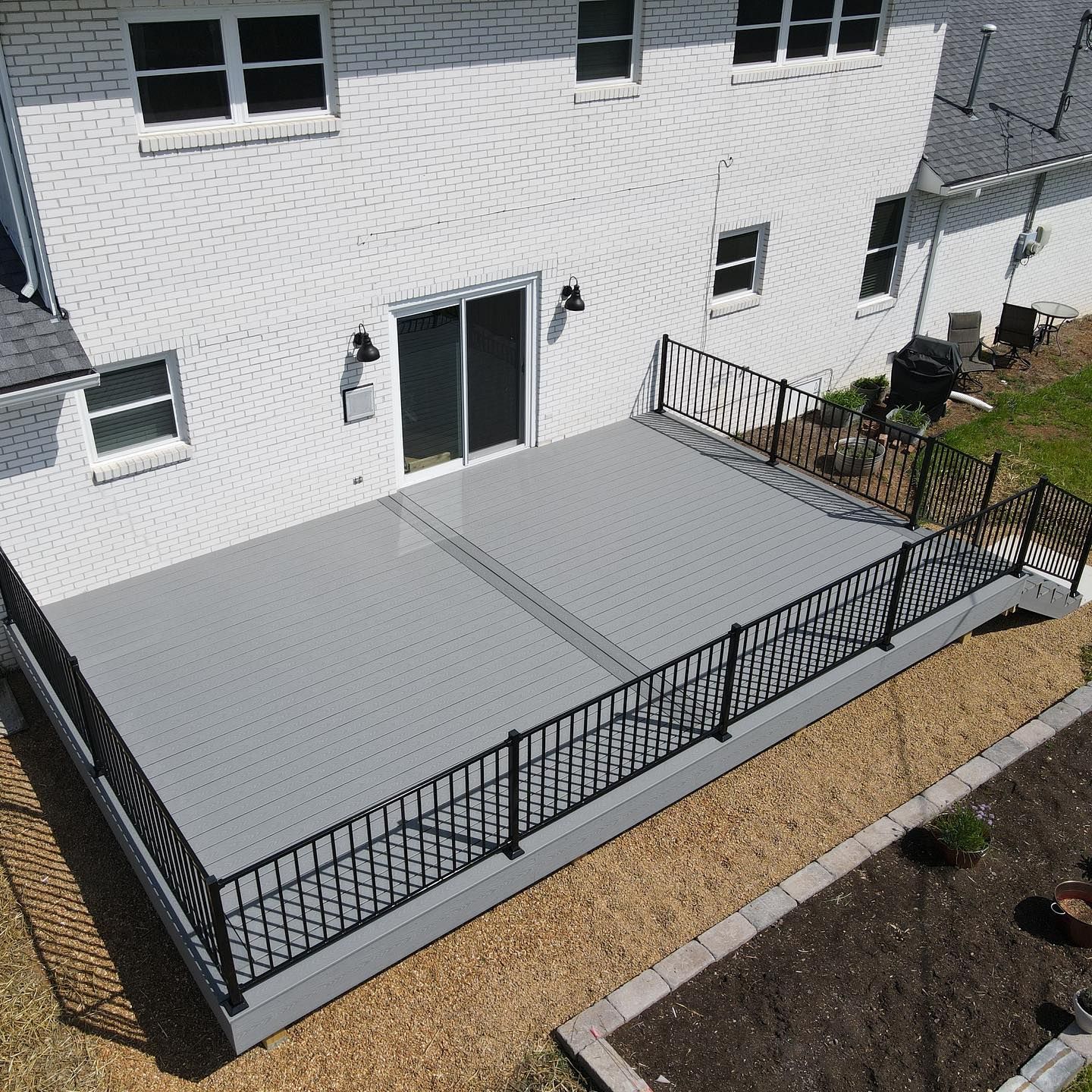 A high-angle view of a grey composite deck with black metal railings attached to a white brick house.