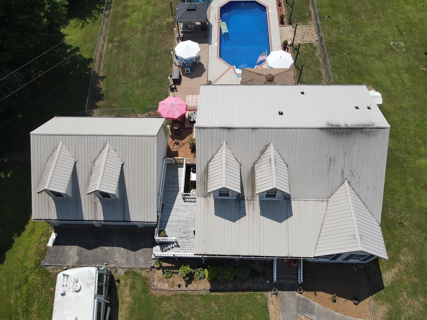 Aerial view of a house with a metal roof, a backyard pool, patio umbrellas, and a recreational vehicle parked nearby.