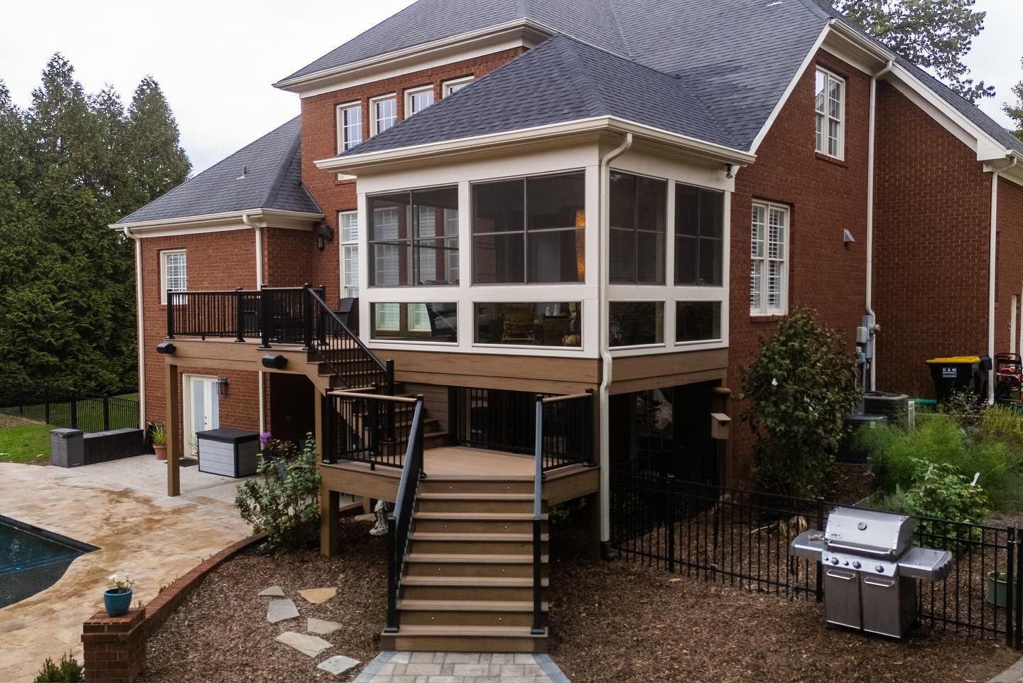 Brick home featuring an elevated screened porch, a wooden deck with black railings, and stone stairs leading to a backyard.