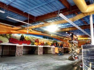Large warehouse interior with colorful mural of vegetables, work in progress.