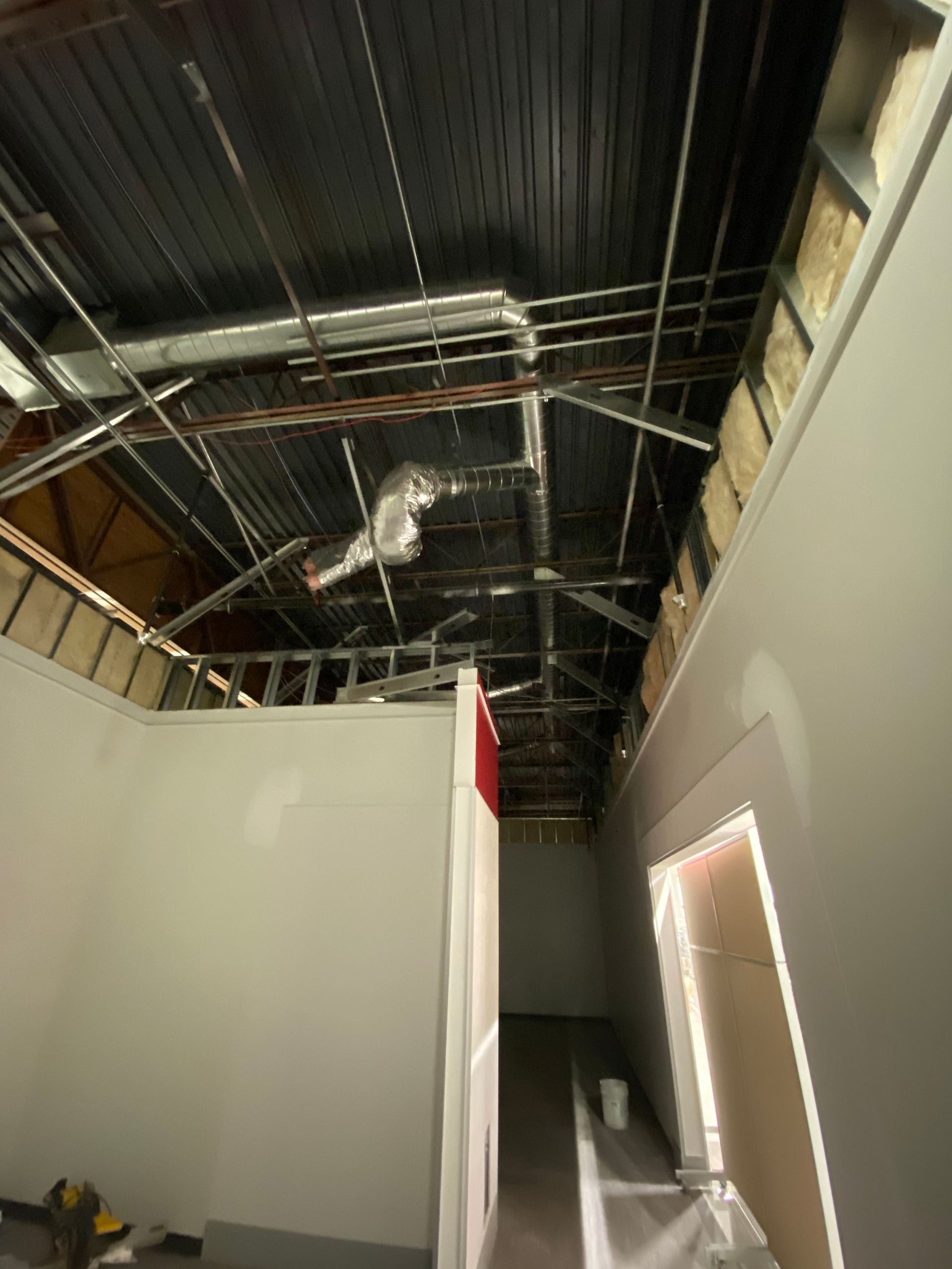 Interior of a building under construction. Exposed ceiling beams and ductwork, drywall walls.