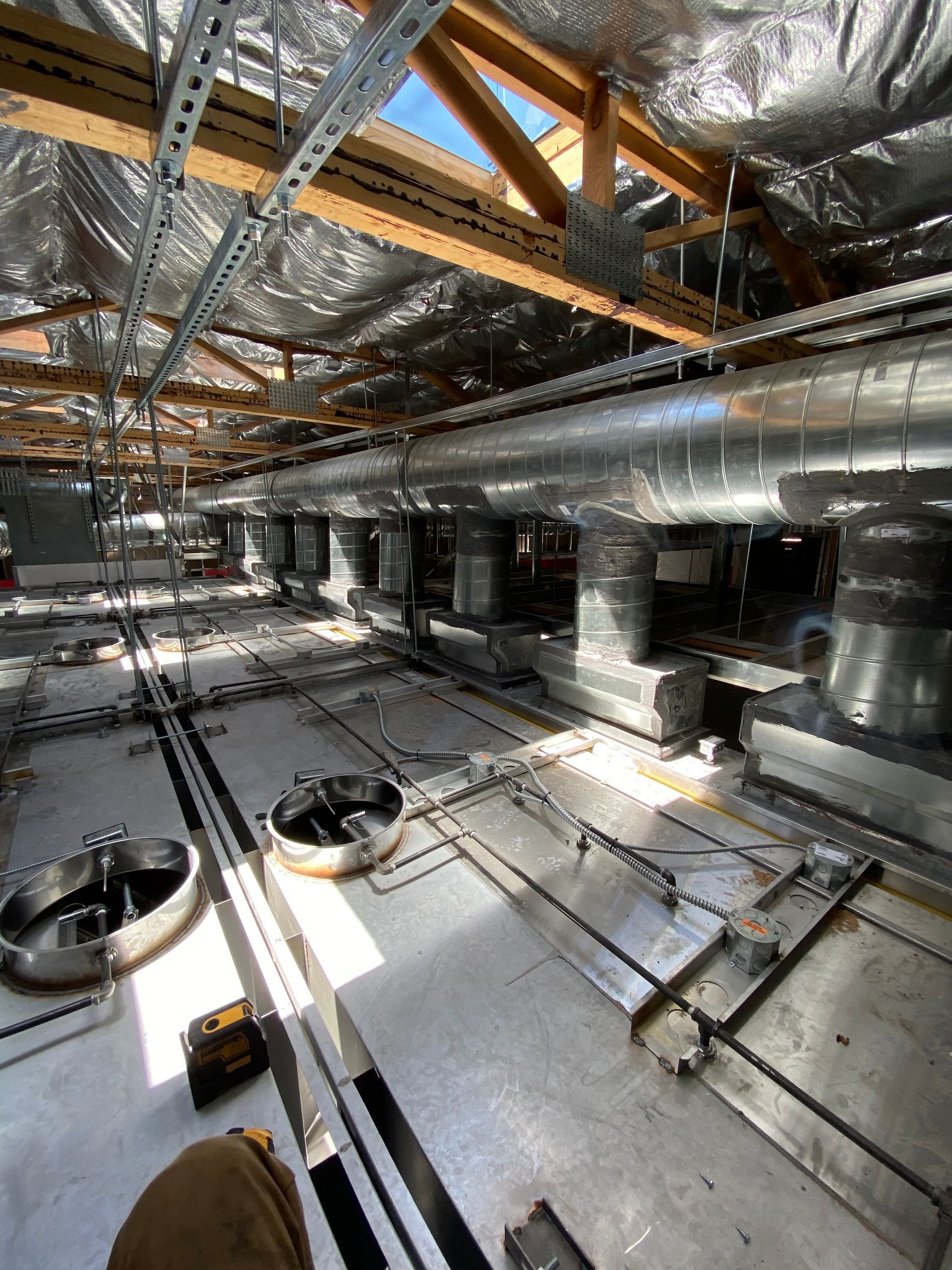 Interior view of a construction site. Metal ductwork, wiring, and insulation are visible on the ceiling and floor.