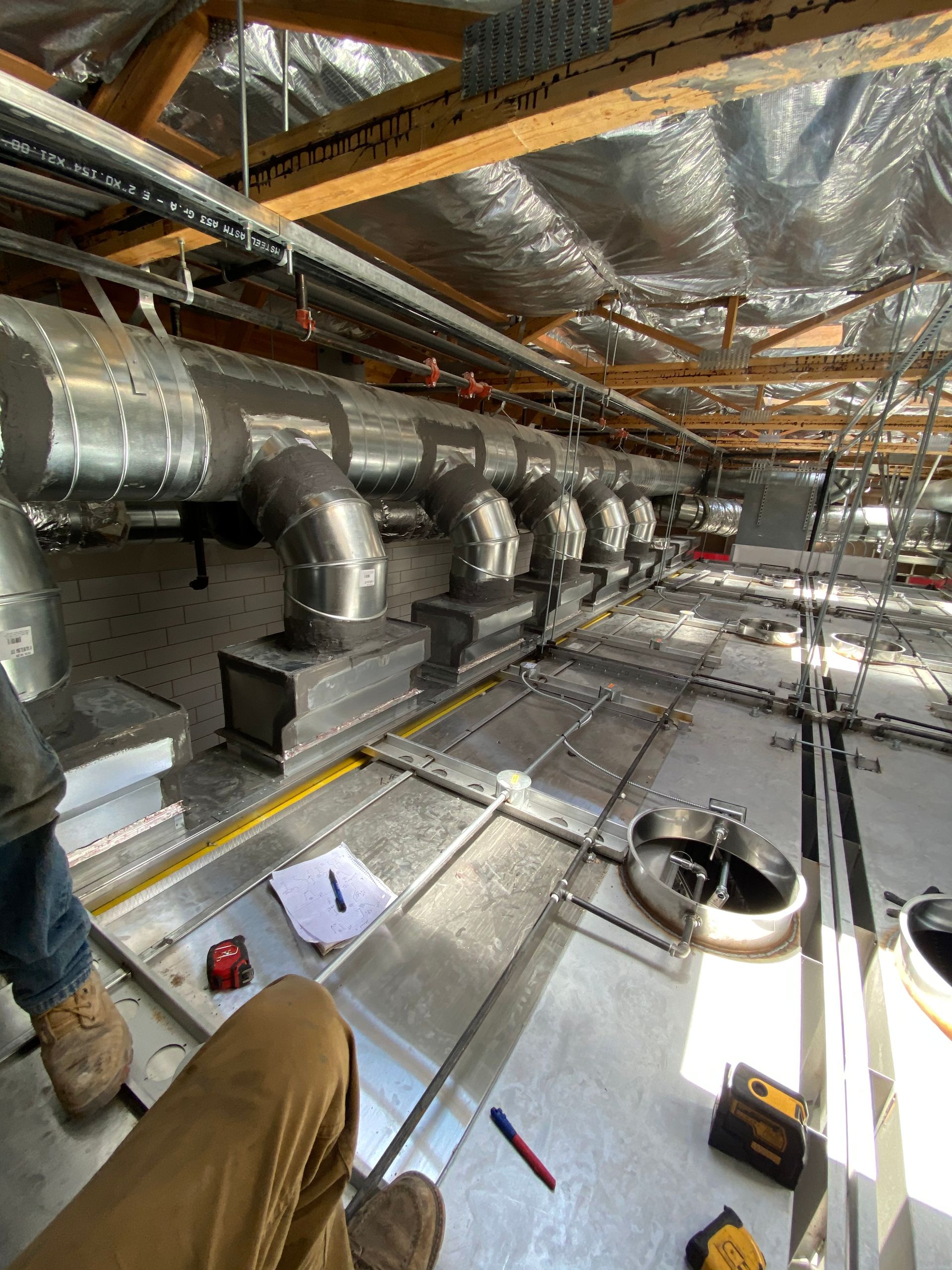 HVAC ductwork installation in a building under construction, with a worker's legs in the foreground.