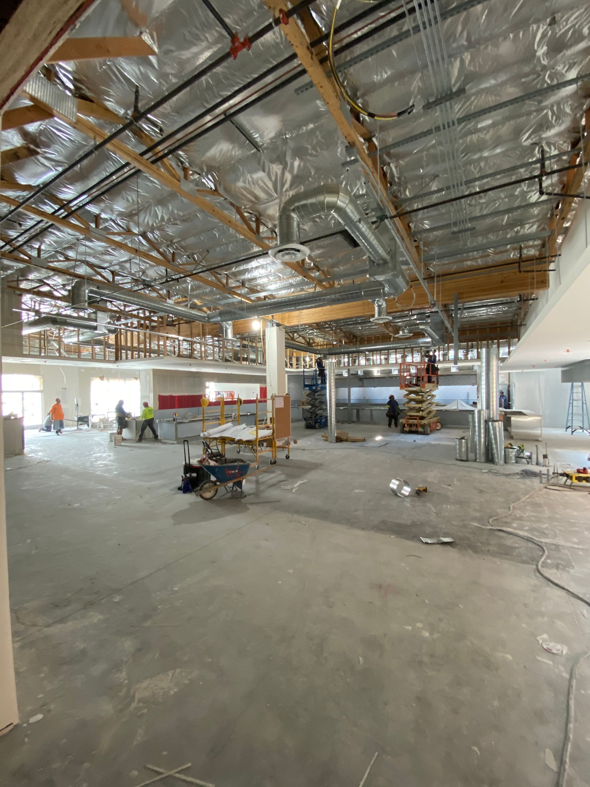 Construction site interior with exposed ceiling, workers, concrete floor.