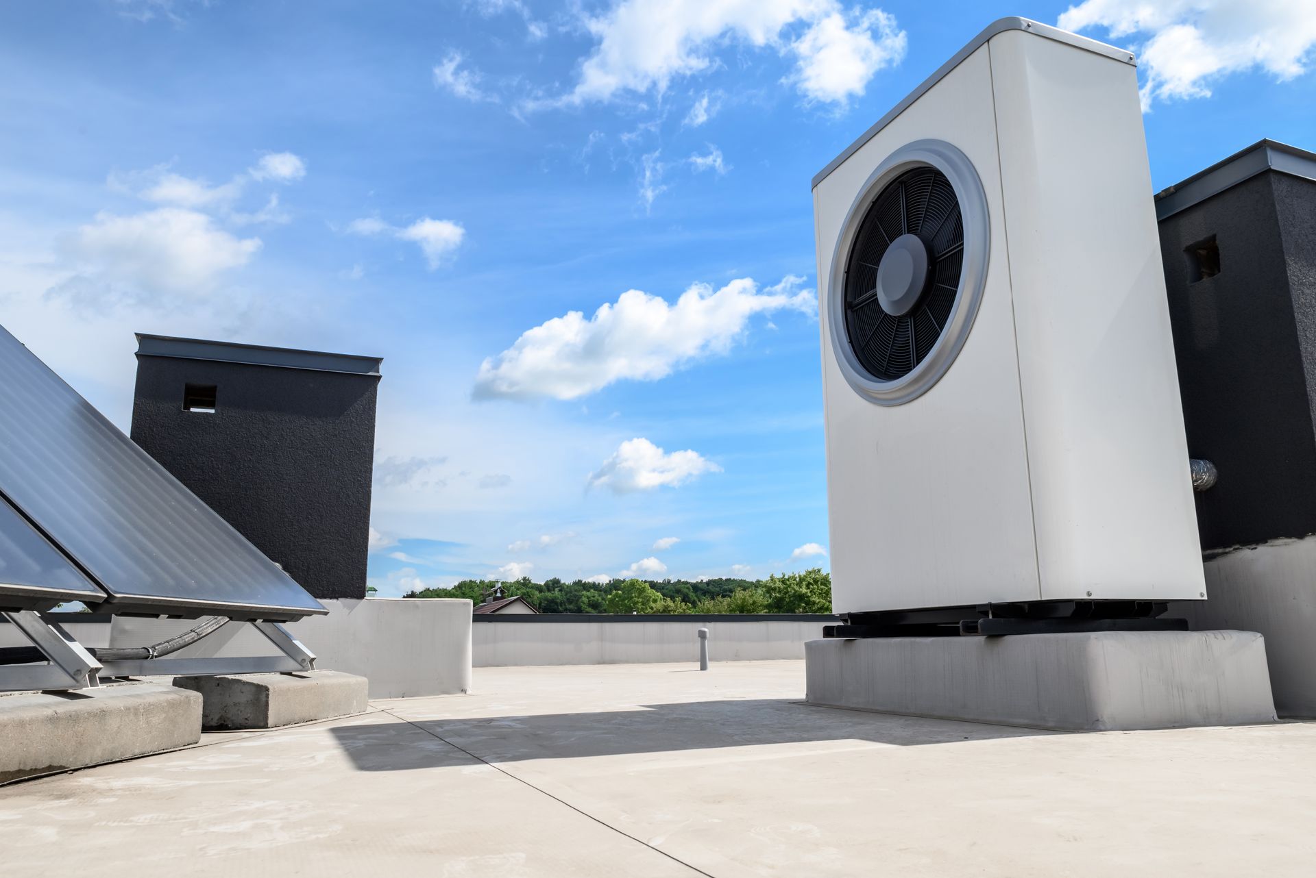 White air conditioning unit on a rooftop with solar panels and chimneys against a blue sky.