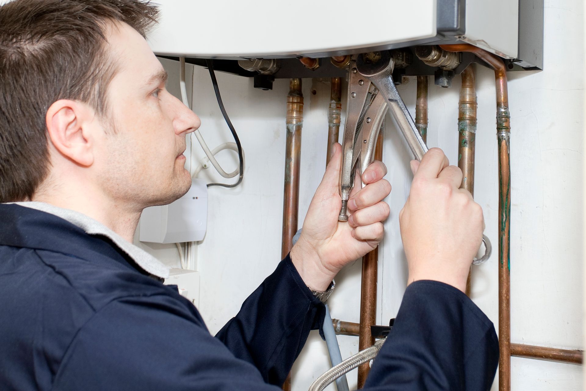 A man is working on a boiler with a pair of pliers.