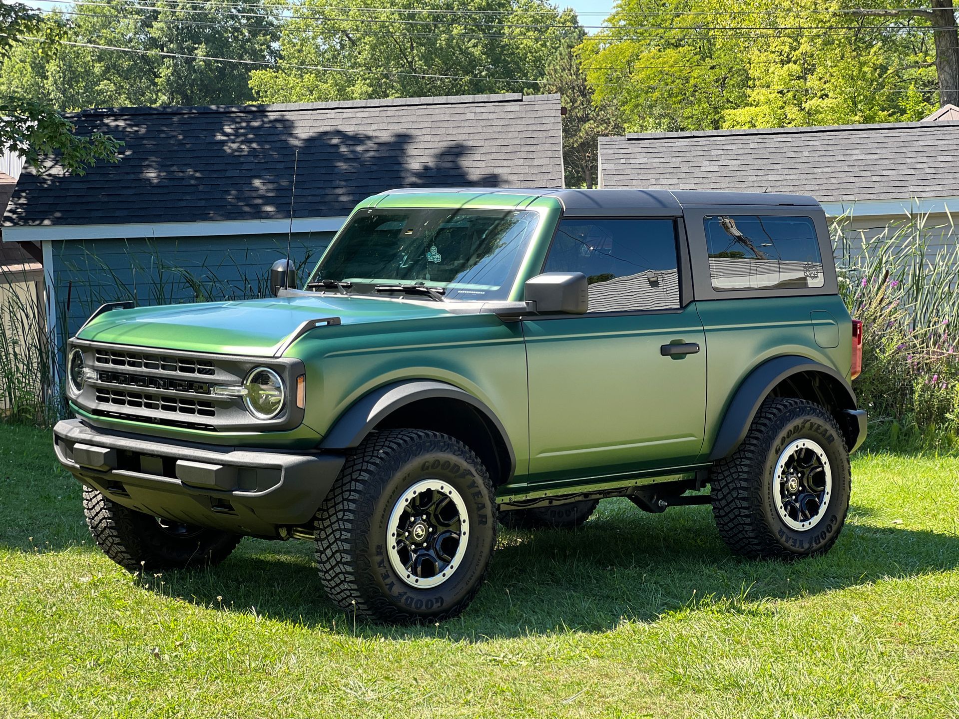 Green Ford Bronco SUV parked on grass with a black roof and black accents.