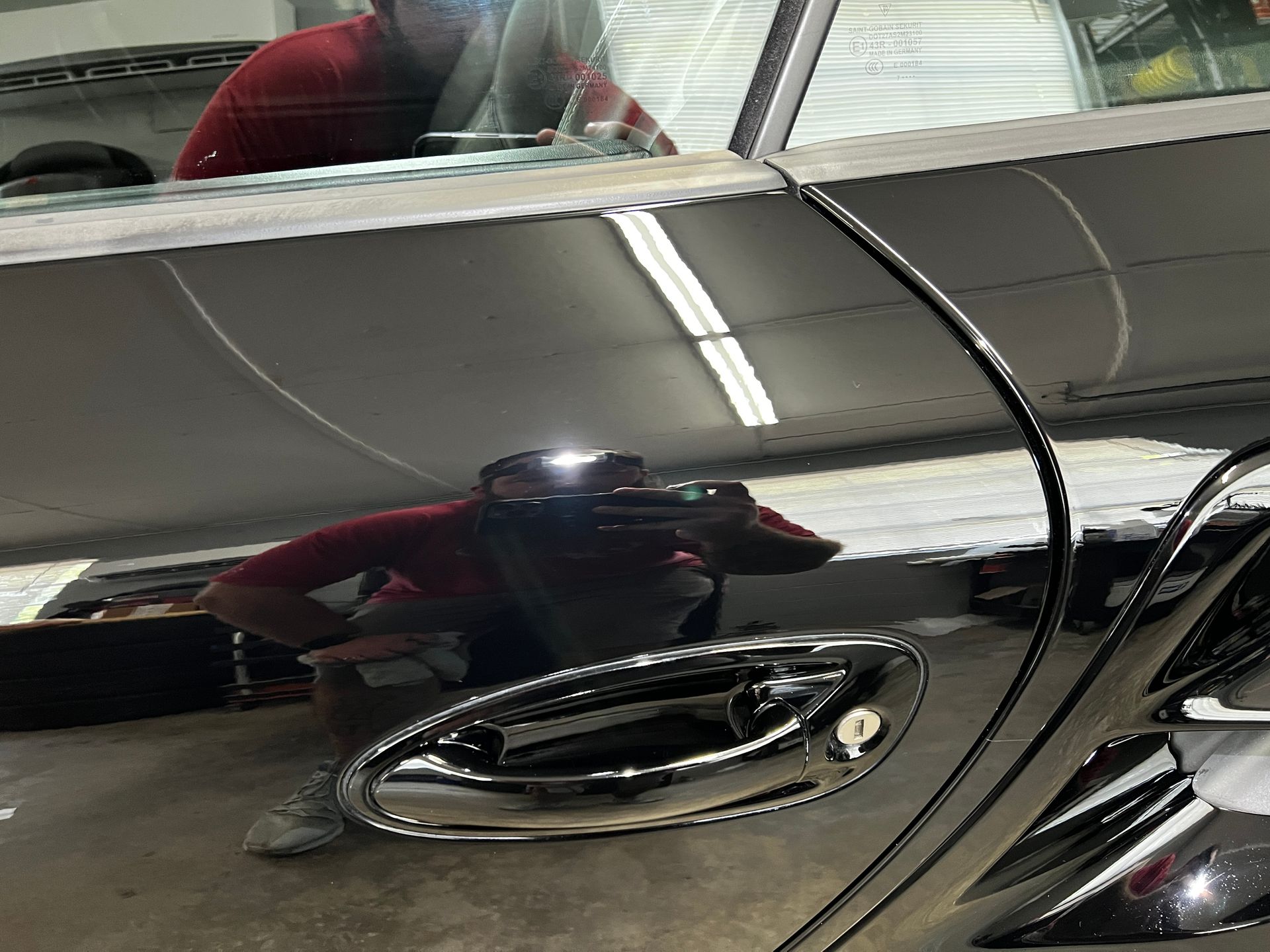 Reflection of a person in red shirt and grey pants working on a shiny car.
