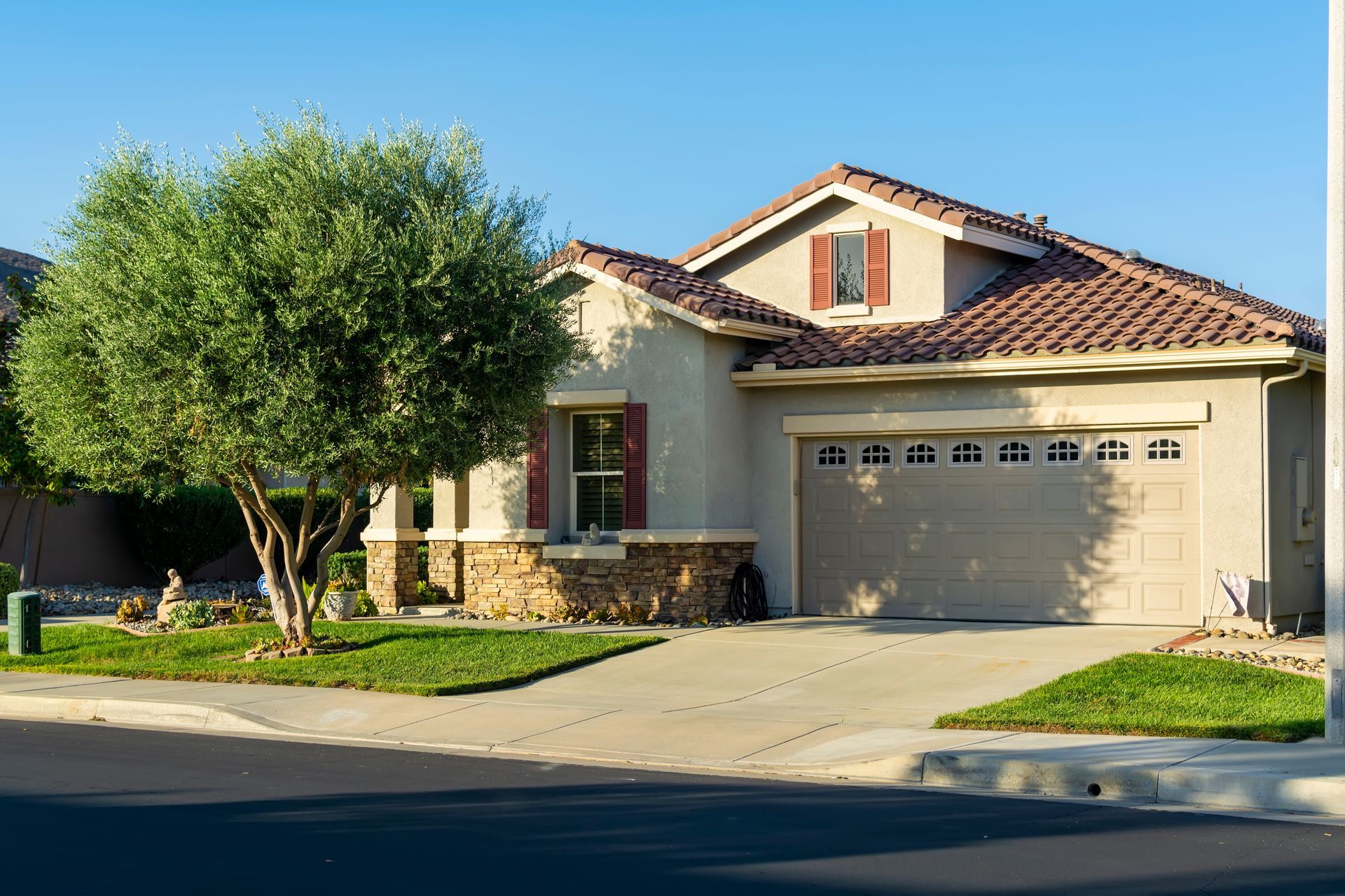 Single-story suburban house with beige exterior, red-tiled roof, garage, and a tree in front yard
