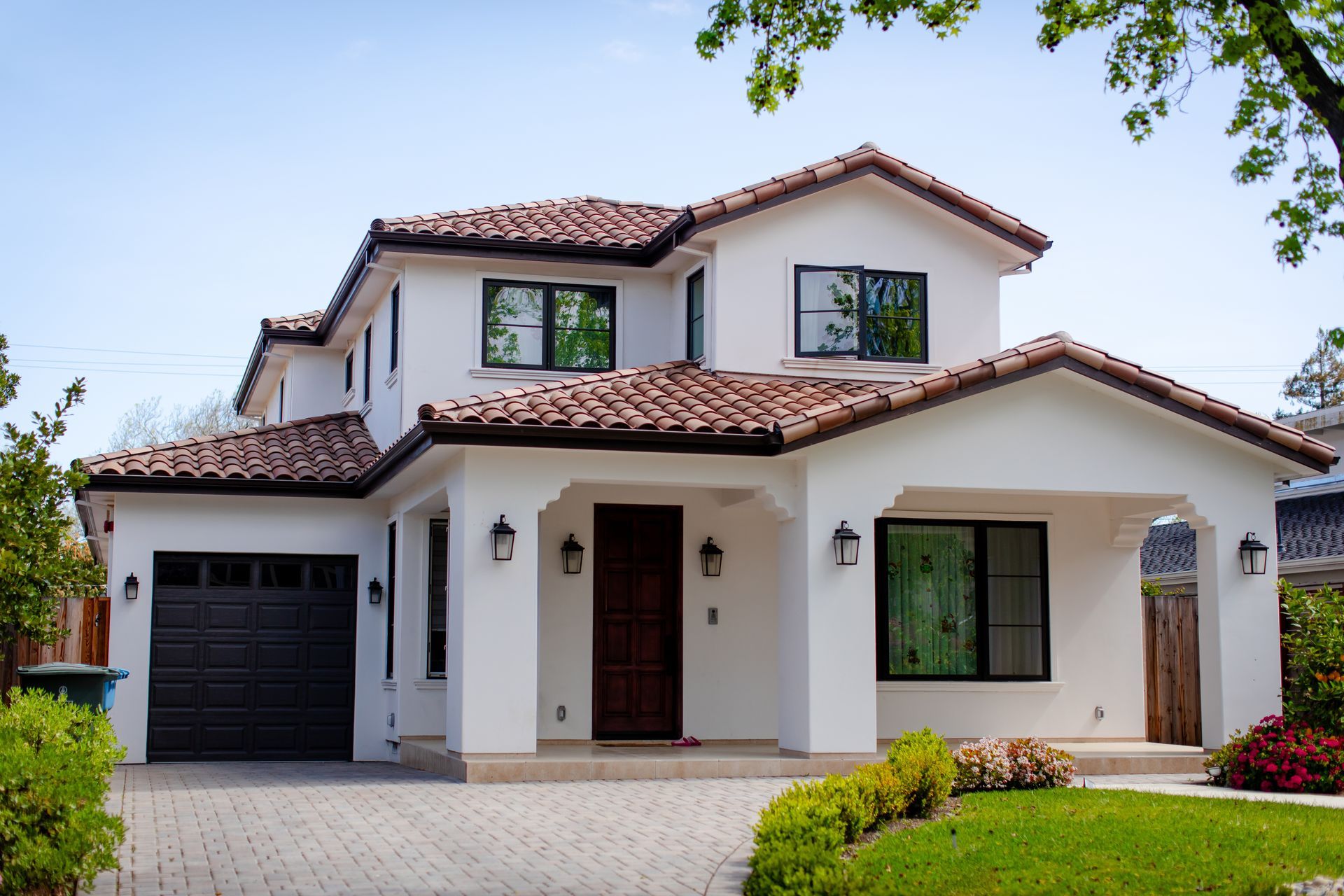 Modern two-story white house with red tile roof, black garage door, and front lawn