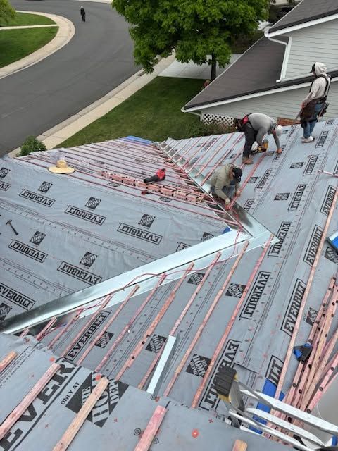 Roofing workers installing underlayment on a sloped house roof with a neighborhood street below.